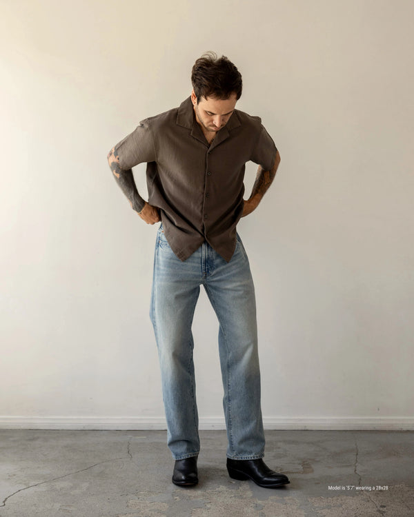 5'7" Man wearing a brown shirt and blue jeans against a plain white wall.