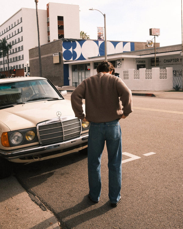 Man standing next to a vintage Mercedes-Benz car on a city street.