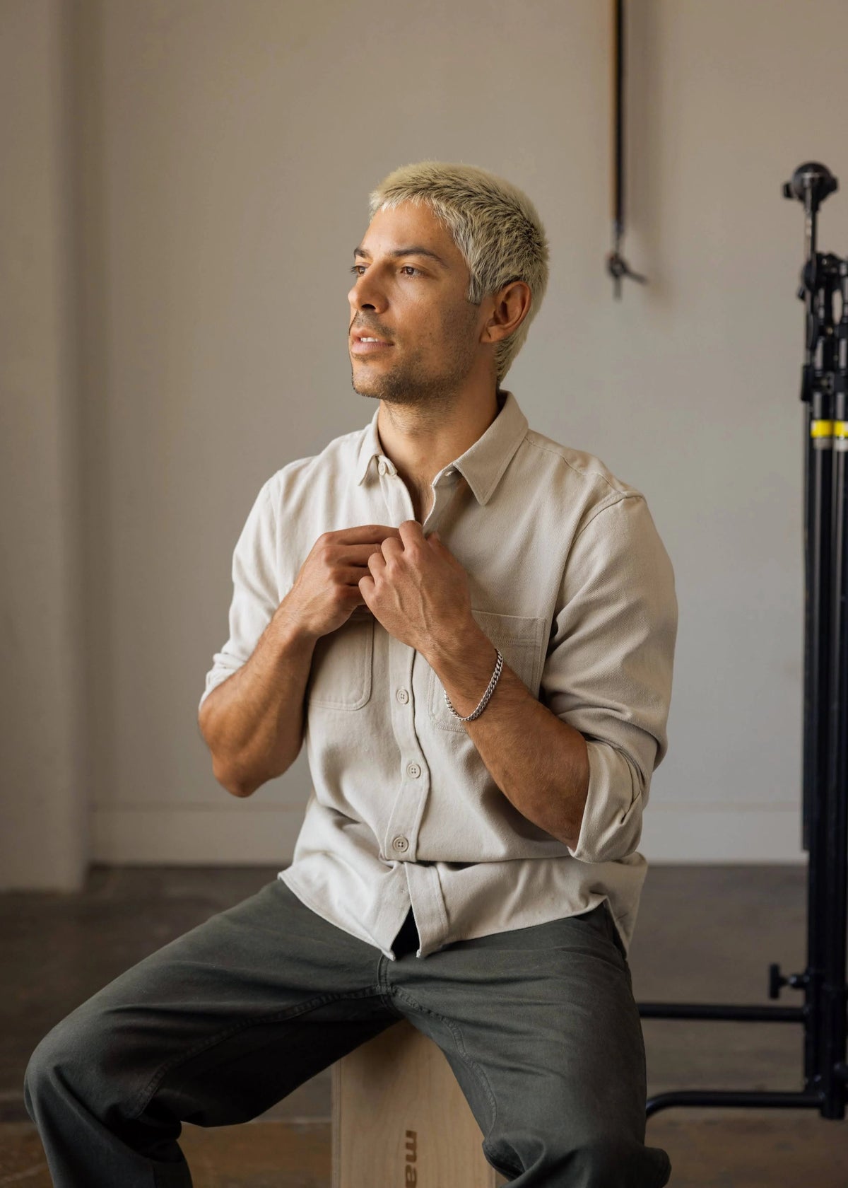 Shorter Man sitting on a stool adjusting his shirt in a neutral setting