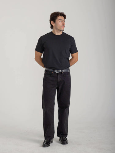 Man wearing a black t-shirt and black jeans on a gray background