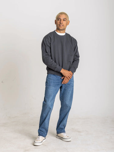 Man wearing a gray sweatshirt and blue jeans standing against a white background