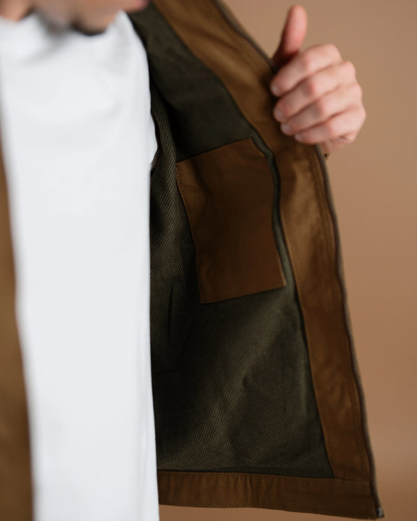 Close-up of a person wearing a brown jacket with a white shirt underneath, holding the jacket open to show the interior lining and a brown patch pocket.