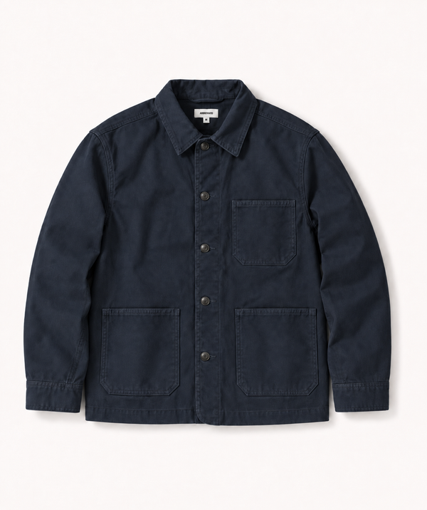 A dark navy blue canvas utility jacket with a button-up front, a chest pocket, and two large front patch pockets, laid flat against a light off-white background.