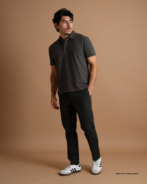 Short man wearing a dark gray Sueded Jersey Polo with black pants against a warm brown background.
