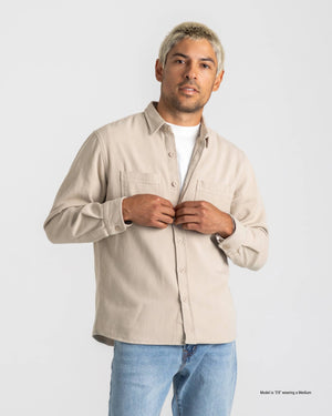 Shorter Man wearing a beige shirt and blue jeans against a white background