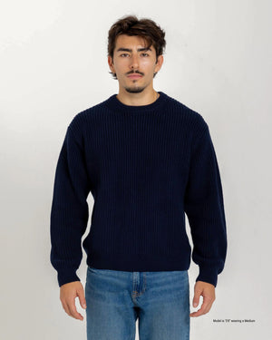 Shorter Man wearing a navy blue sweater and jeans against a white background