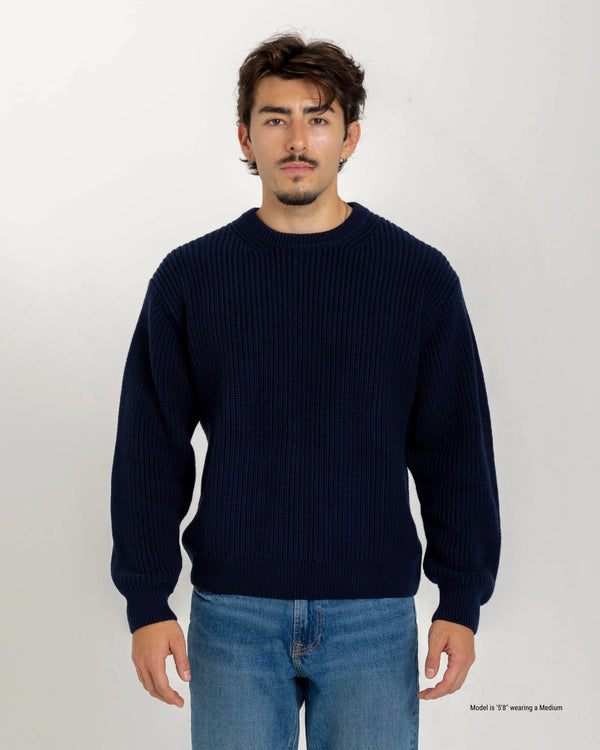 Shorter Man wearing a navy blue sweater and jeans against a white background