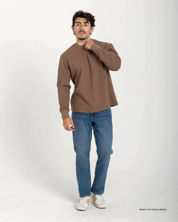 Man wearing a brown sweater and blue jeans on a white background