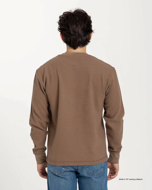 Man wearing a brown long-sleeve shirt and blue jeans on a white background