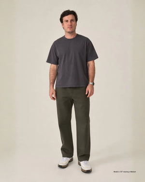 A man modeling a dark charcoal gray crewneck t-shirt and olive green pants against a plain beige studio background.