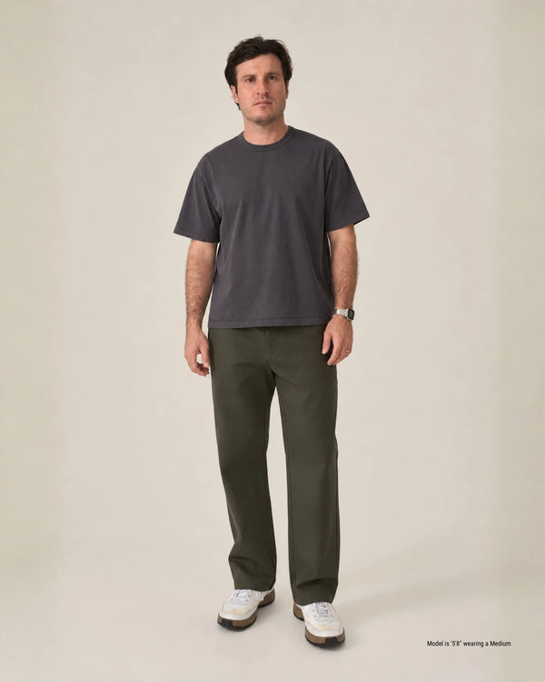 A man modeling a dark charcoal gray crewneck t-shirt and olive green pants against a plain beige studio background.