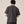 Load image into Gallery viewer, A man viewed from behind wearing a dark charcoal gray short-sleeve t-shirt and dark brown pants, standing against a plain beige studio background.
