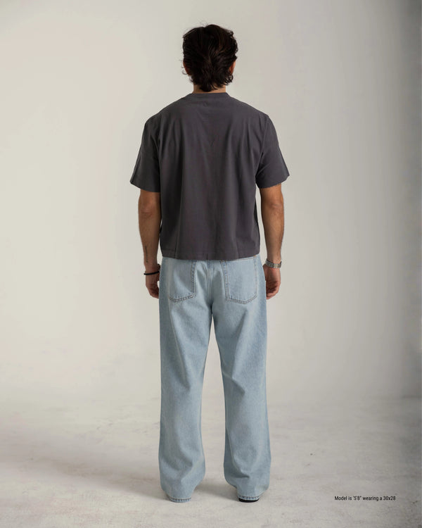 Short male Person wearing a dark gray t-shirt and light blue jeans against a plain background