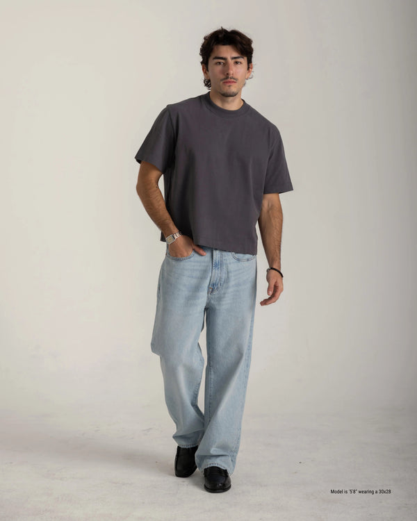 Shorter Man wearing a gray t-shirt and light blue jeans on a plain background