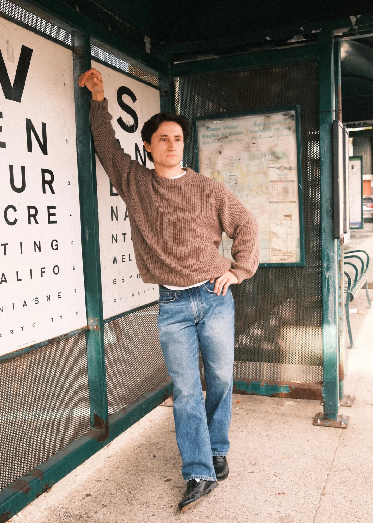 Short Man standing in a bus stop with a large eye chart in the background