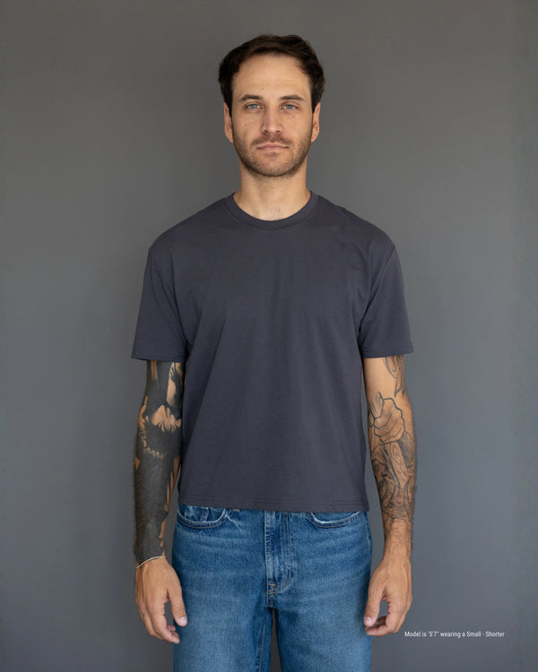 Man wearing a plain dark gray t-shirt and blue jeans against a gray background