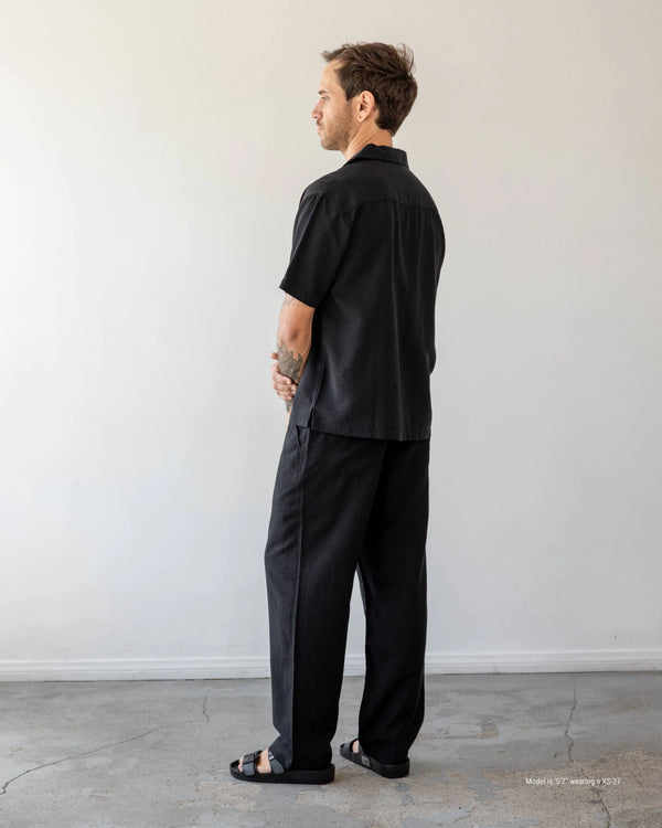 Man wearing a black outfit standing against a white wall.