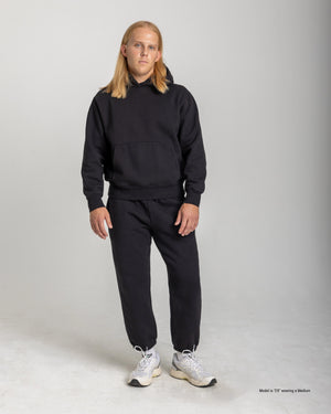 A short man wearing Black Cinched-Hem Sweatpants with a black hoodie and white sneakers, showing the relaxed fit and cinched ankles against a light studio background.