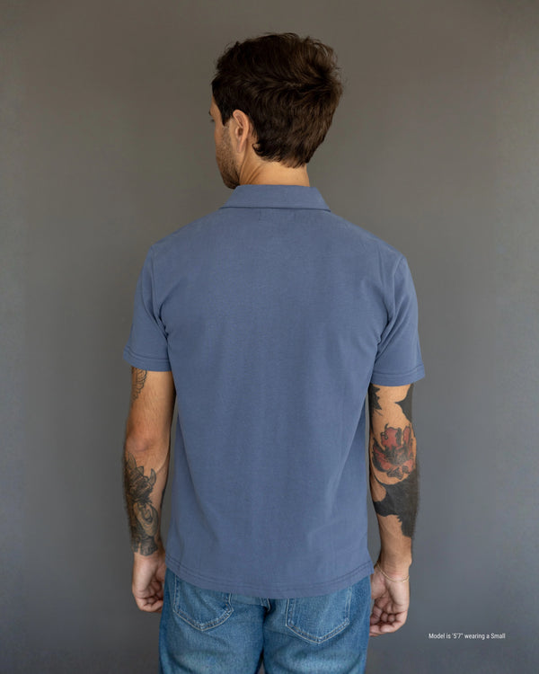 5'7" Man wearing a blue polo shirt and jeans against a gray background