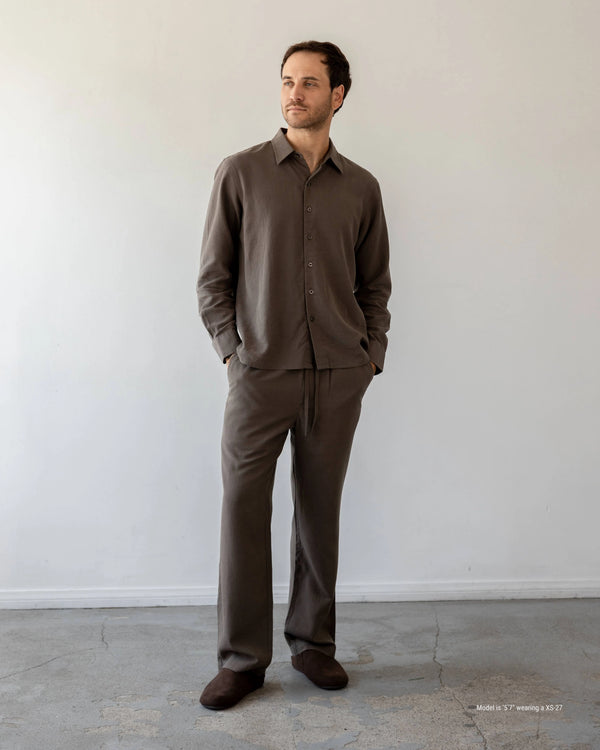 Man wearing a brown outfit standing against a white wall.