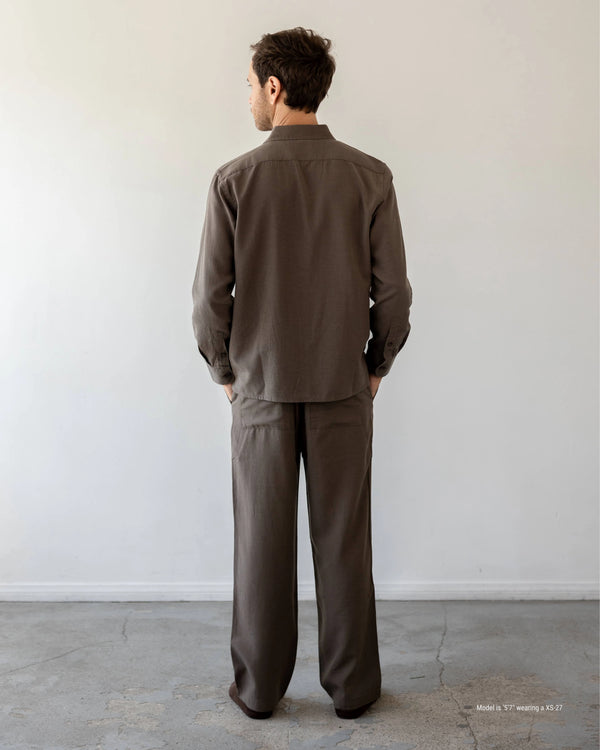 Man wearing a brown outfit standing against a plain white wall.