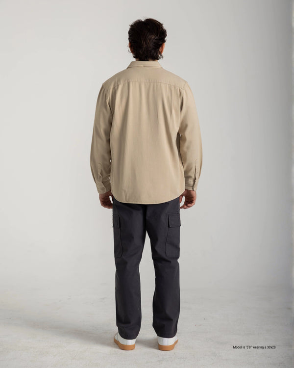 Person wearing a beige shirt and dark pants on a plain background