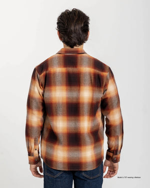 A short man shown from the back wearing a Rust Heavyweight Waffle Knit Crew with dark indigo jeans, highlighting the brown, rust orange, cream, and gray plaid pattern against a white studio background.
