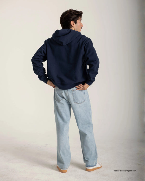 Person wearing a navy hoodie and light blue jeans on a plain background