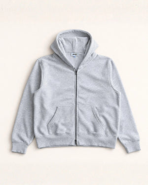 Man wearing a blue hoodie and gray pants standing in a minimalistic room.