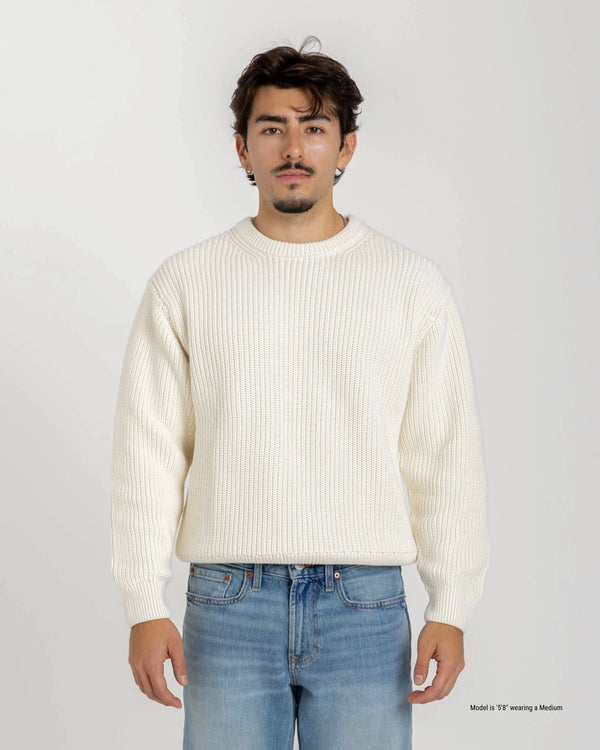 Short Man wearing a cream sweater and light blue jeans against a white background