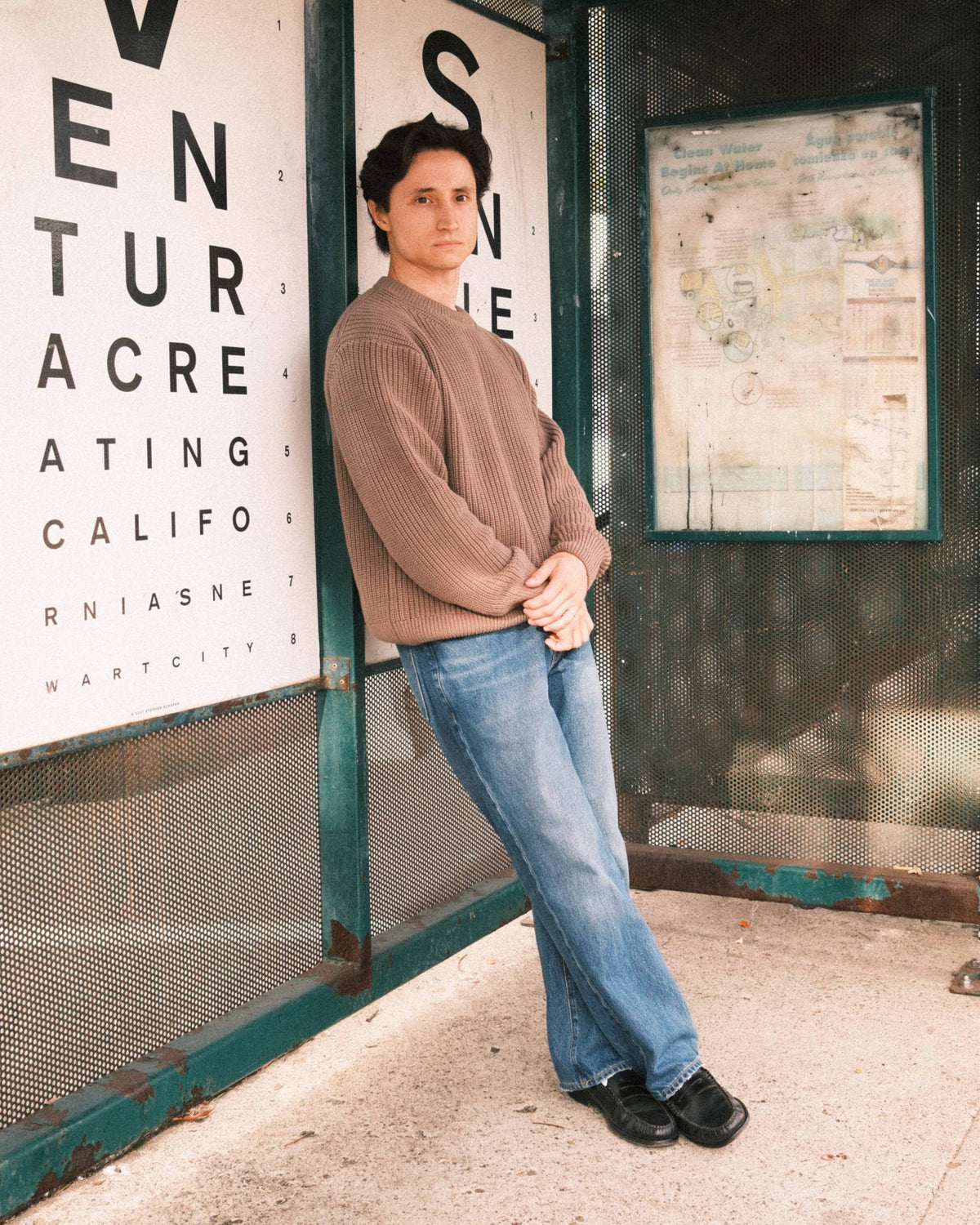 Person leaning against a wall with an eye chart and advertisement in the background