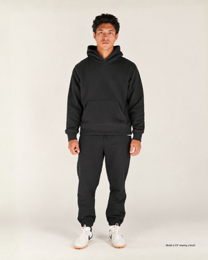 Shorter man wearing black jogger sweatpants with a black hoodie and white sneakers, front view showing the tapered leg, drawstring waist and elastic ankle cuffs