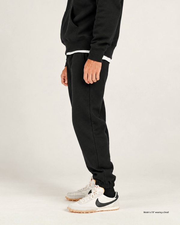Side view of black jogger sweatpants for shorter men, showing the tapered fit from hip to cuffed ankle with white sneakers