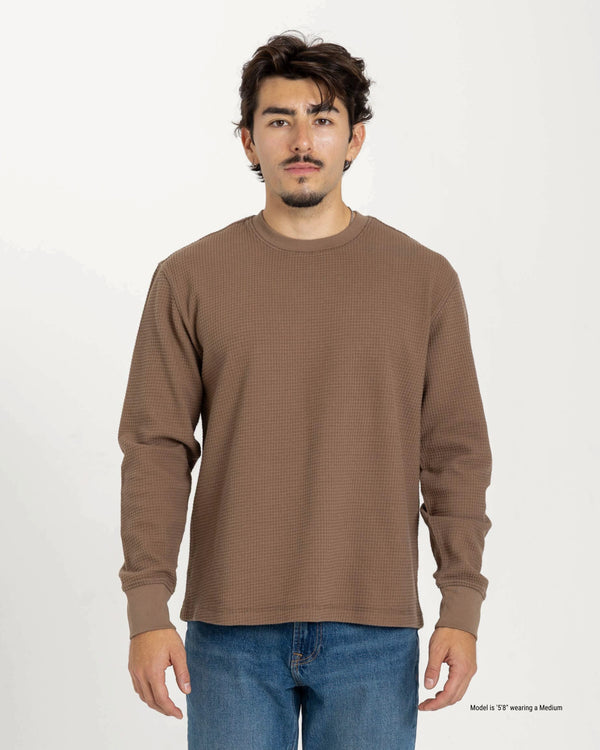 Man wearing a brown long-sleeve shirt and blue jeans on a white background