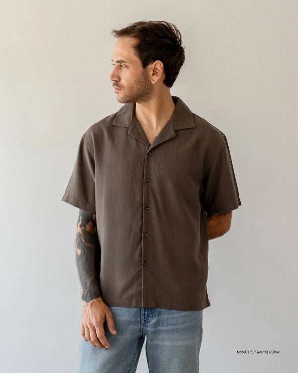 Shorter Man wearing a brown short-sleeve shirt and blue jeans against a plain background