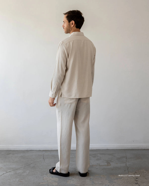 Man wearing a beige suit standing against a plain white wall.