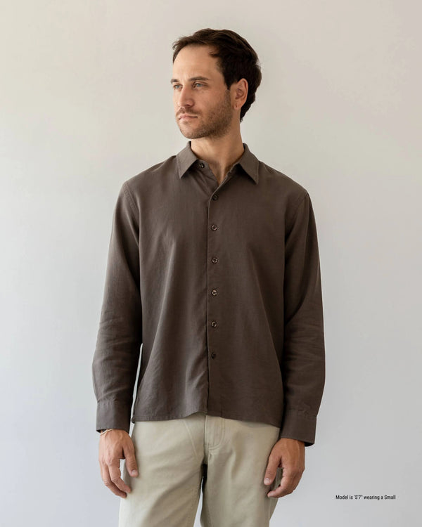 Man wearing a brown button-up shirt and beige pants against a plain background
