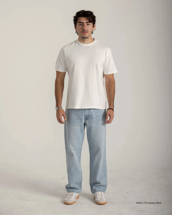 Man wearing a plain white t-shirt and light blue jeans on a gray background