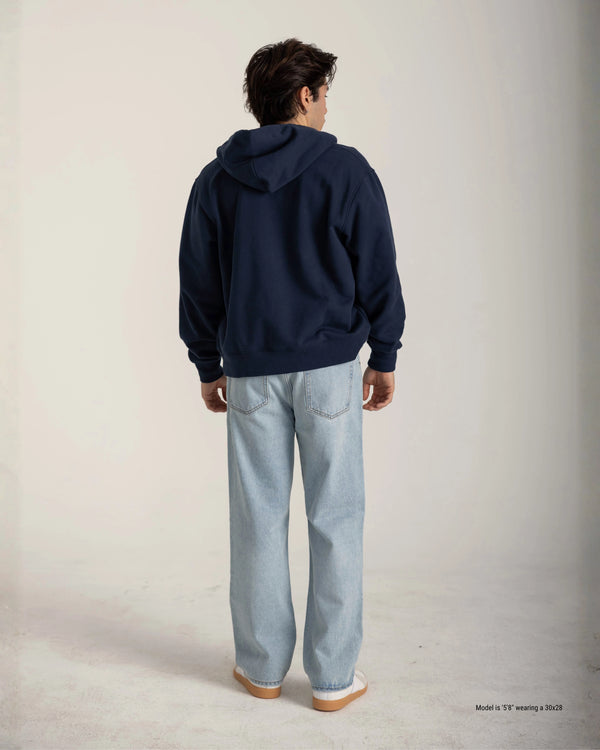 Person wearing a navy hoodie and light blue jeans on a plain background