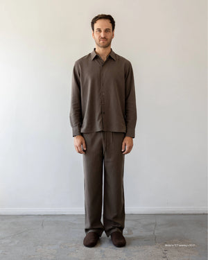 Man wearing a black outfit standing against a plain white wall.