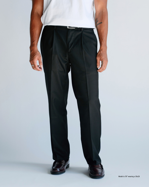 Front view of black loose-fit pleated trousers from waist to loafers, showing the relaxed straight leg on a shorter man
