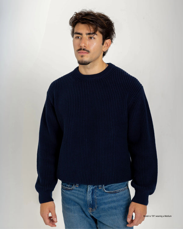 Short Man wearing a navy sweater and blue jeans against a white background