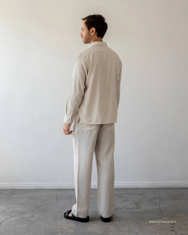 Man wearing a beige suit standing against a plain white wall.