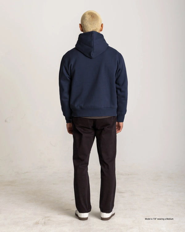 Person wearing a navy blue hoodie and dark pants on a light background