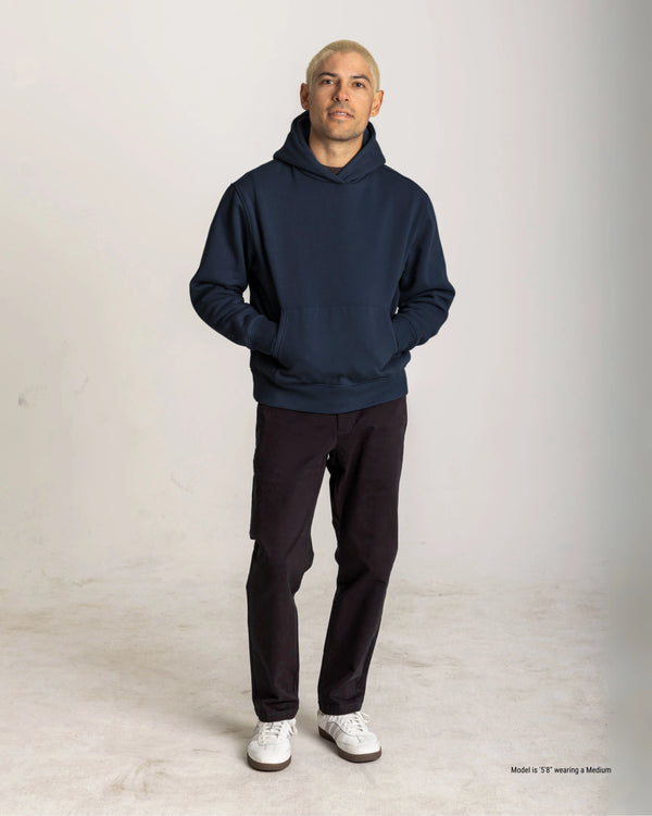 Man wearing a navy hoodie and black pants on a light gray background