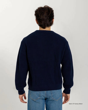A short man shown from the back wearing a Deepwater navy Cotton Fisherman Sweater with light blue jeans, highlighting the ribbed knit texture and proportional fit against a white studio background.
