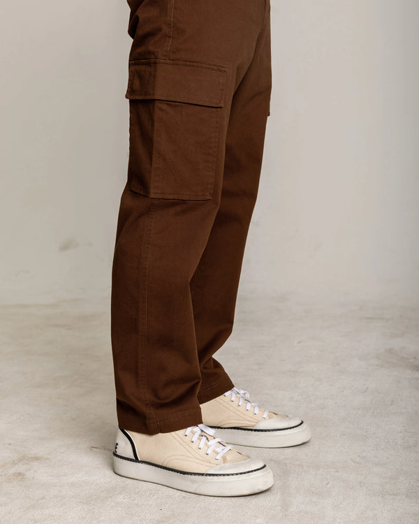 Brown cargo pants worn with white sneakers on a neutral background