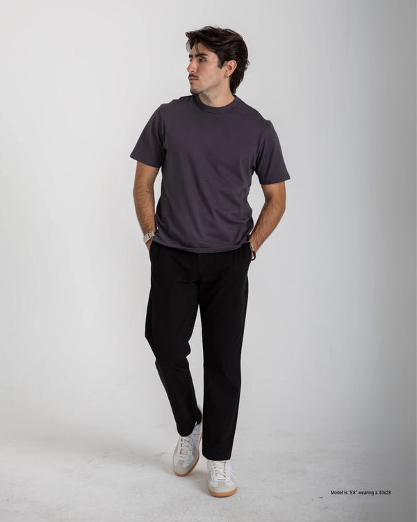 Man wearing a dark gray t-shirt and black pants on a white background
