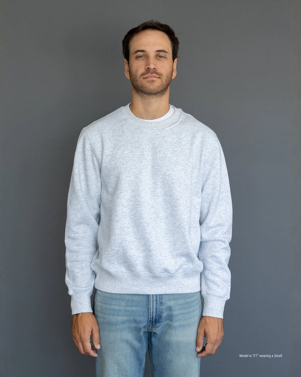 Shorter Man wearing a light gray sweatshirt and blue jeans against a plain background