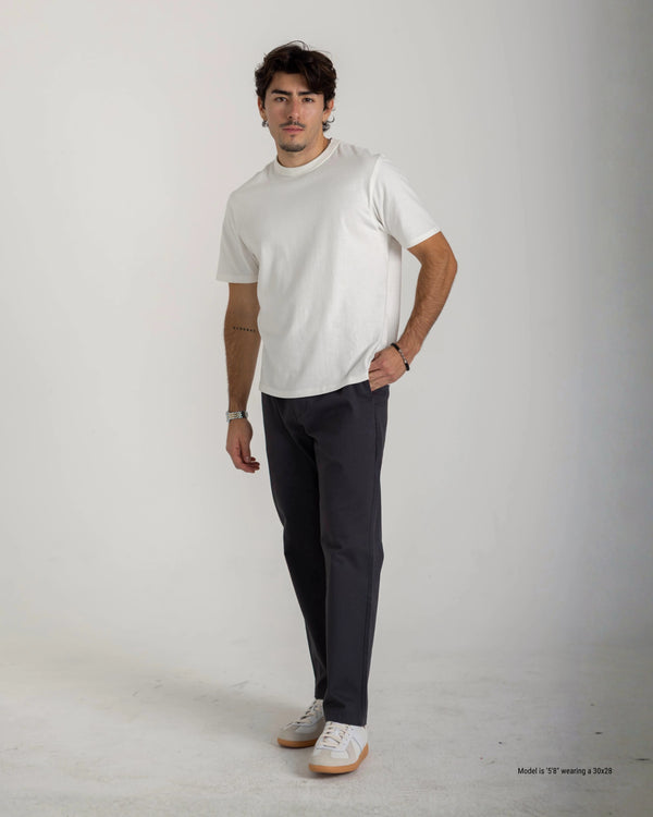 Man wearing a white t-shirt and dark pants on a plain background